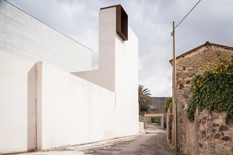 Complesso parrocchiale di Santa Chiara “si colloca nell’area centrale del piccolo abitato di Sini, nella Sardegna interna, con rigore formale e consapevolezza contestuale, cogliendo l’occasione per ricucire una serie di elementi spaziali, espressivi e relazionali del tessuto centrale. Interpretando elementi tipici dell’edilizia spontanea locale e di un’architettura sobria della koiné mediterranea, il progetto agisce in un contesto difficile per rinnovare i nessi di senso con le comunità.”