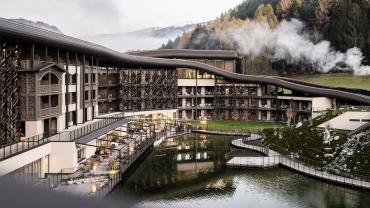 La soluzione di NOA, che ha progettato la nuova struttura, a sorpresa è partita dal tetto: alla tradizionale copertura a falda del vecchio complesso alberghiero si è sostituita un’ampia struttura a onda che riveste edifici nuovi e preesistenti, degradando sui due lati fino a sparire nel terreno. Una sorta di collina, quindi, che si integra con il paesaggio coprendosi di vegetazione, e che diventa pista da sci, di pattinaggio, campo da gioco, parco avventura, zona di svago e di ricreazione.