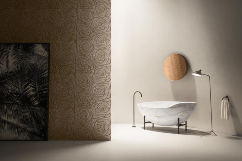 KORA &amp; ROSE: la vasca Kora, scavata in un blocco di marmo fino a ottenere una forma avvolgente, sembra librarsi nell&rsquo;aria, sostenuta da una sottile struttura in metallo; il decoro stilizzato di Rose, crea una texture grafica sulla parete, con un&rsquo;unica linea che si rincorre.